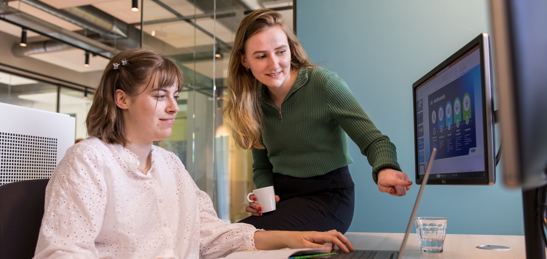 twee vrouwen kijkend naar laptop en beeldscherm